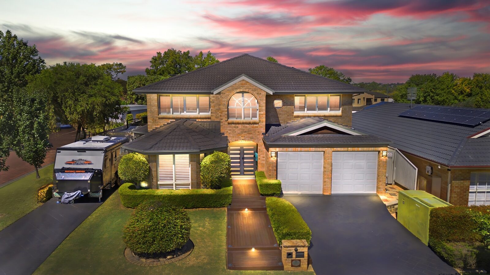 Large two-story house with illuminated pathway at dramatic sunset.